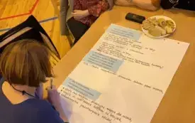 Na zdjęciu ludzie siedzą przy stołach rozmawiają.