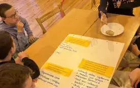 Na zdjęciu ludzie siedzą przy stołach rozmawiają.