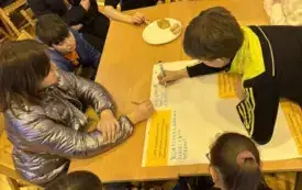 Na zdjęciu ludzie siedzą przy stołach rozmawiają.