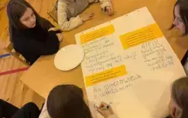 Na zdjęciu ludzie siedzą przy stołach rozmawiają.