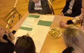 Na zdjęciu ludzie siedzą przy stołach rozmawiają.