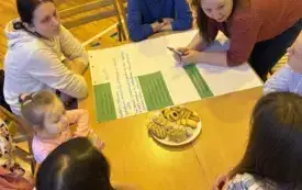 Na zdjęciu ludzie siedzą przy stołach rozmawiają.