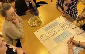 Na zdjęciu ludzie siedzą przy stołach rozmawiają.