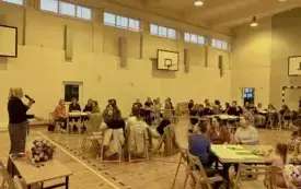 Na zdjęciu ludzie siedzą przy stołach rozmawiają.