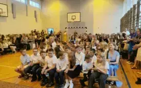Na zdjęciu uczniowie siedzą w sali gimnastycznej. Ubrani galowo.