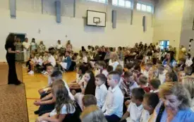 Na zdjęciu uczniowie siedzą w sali gimnastycznej. Ubrani galowo.