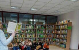 Zdjęcie przedstawia uczni&oacute;w, kt&oacute;rzy siedzą na tle p&oacute;łek z książkami.