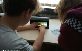 Zdjęcie przedstawia uczni&oacute;w, kt&oacute;rzy sprawdzają banknoty w świetle UV.