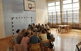 Na zdjęciuludzie siedzą przy stołach na duzej sali.