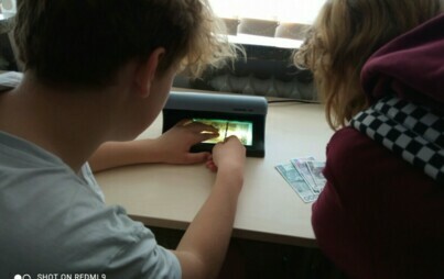 Na zdjęciu uczniowie sprawdzają banknoty pod światłem UV.