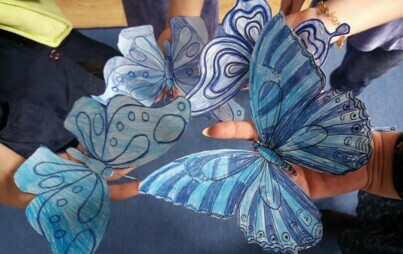 Na zdjęciu dzieci trzymają w dłoniach niebieskie motyle